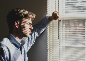person near clear glass window pane and window blinds low-light photography